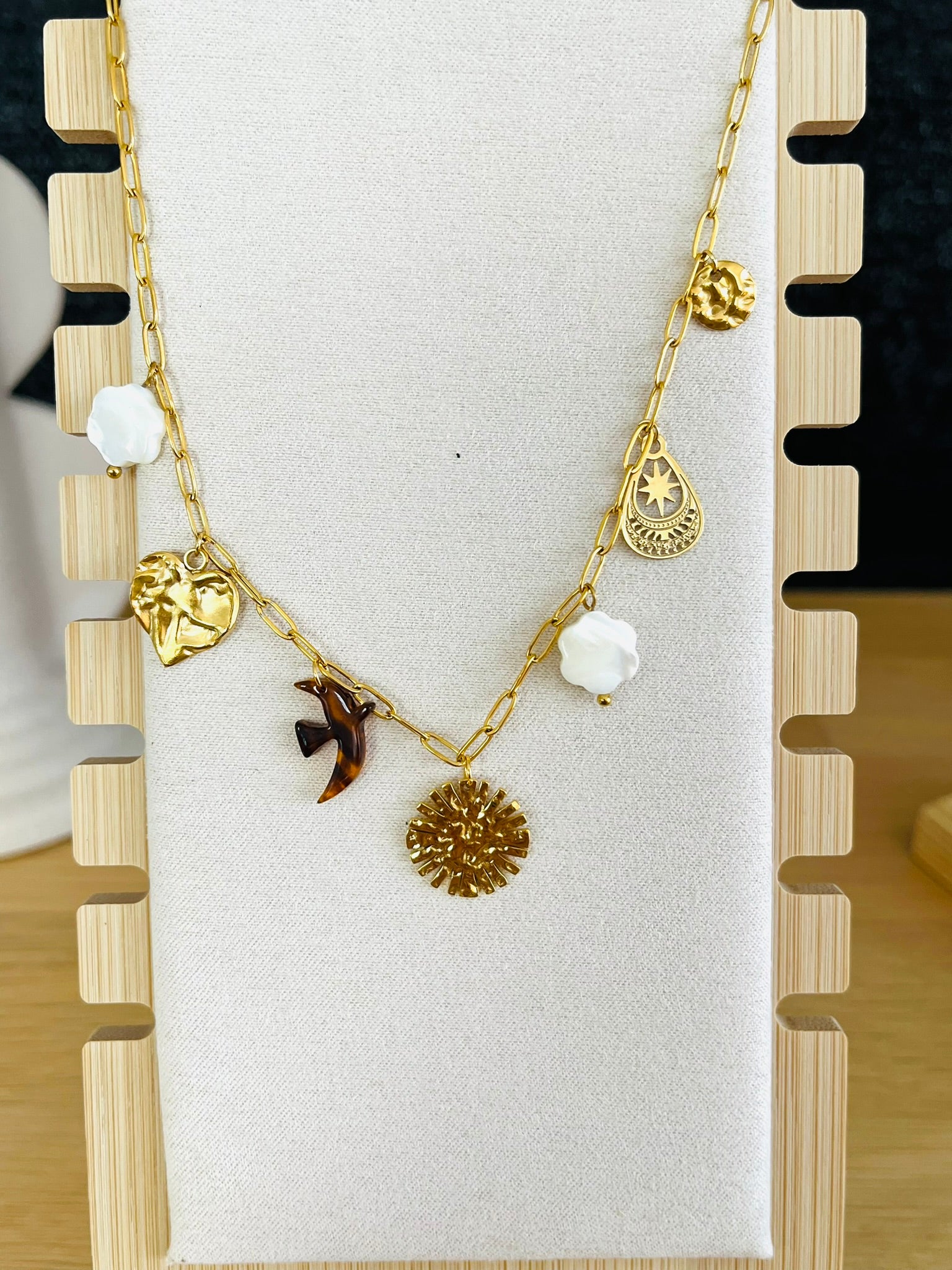 Collier fantaisie fait main.
Collier court en acier inoxydable doré avec 7 charms: fleurs en nacre, soleil, coeur, oiseau en résine, goutte ethnique, sequin martelé.
Bijou fantaisie fait main