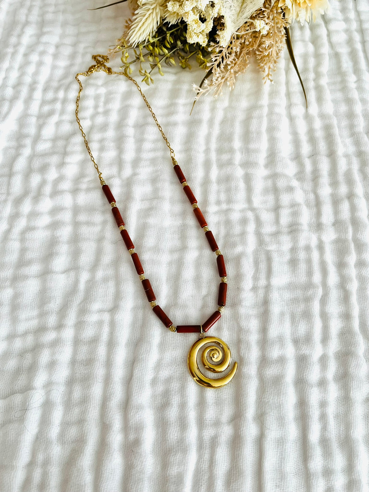 Collier fantaisie fait main.
Chaîne en acier doré et perles tubes en pierre naturelle jaspe rouge rouille.
Pendentif spirale en acier inox doré.
Bijou fait main.