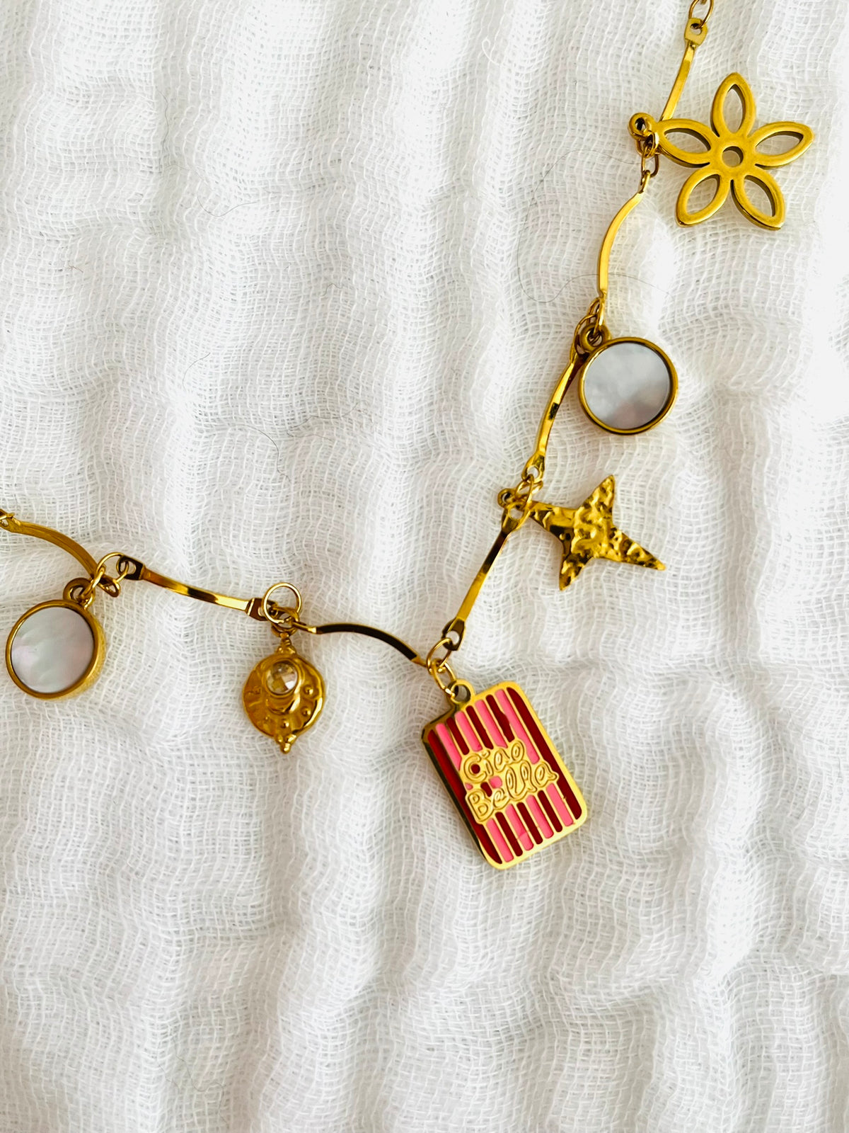Collier fantaisie fait main.
Collier en acier inoxydable avec pampilles en nacre. Fleur, étoile, trèfle, limule en acier doré.
Pendentif central rectangle rayé rouge et rose gravé "Ciao Bella"