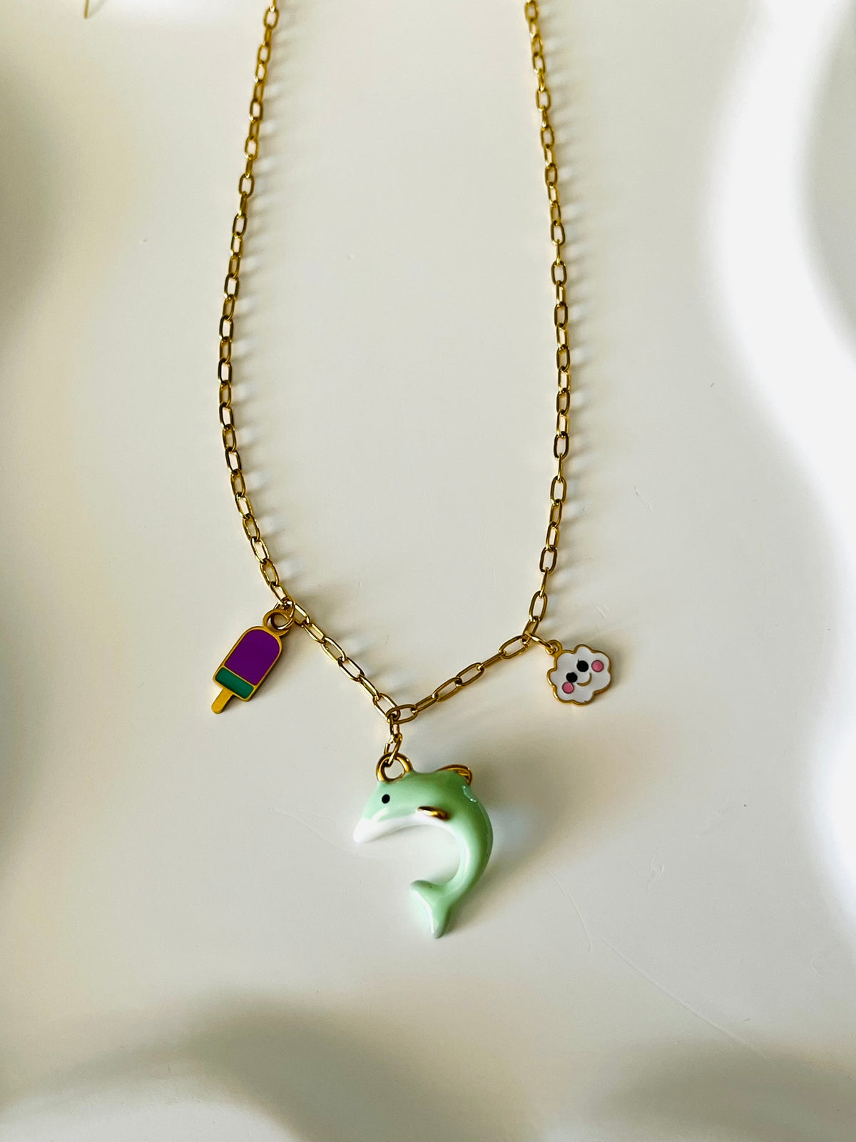 Collier adapté pour les enfants à partir de 6 ans.
Collier en acier inoxydable doré, hypoallergénique.
Breloques dauphin vert d'eau, nuage blanc et glace violet.
