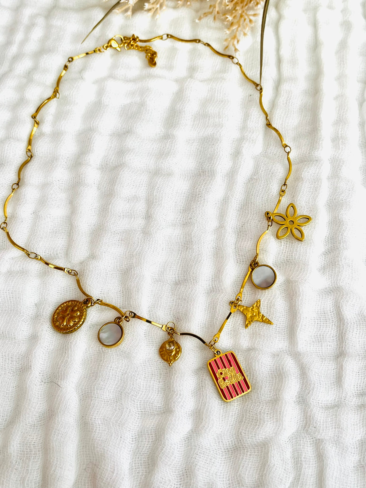 Collier fantaisie fait main.
Collier en acier inoxydable avec pampilles en nacre. Fleur, étoile, trèfle, limule en acier doré.
Pendentif central rectangle rayé rouge et rose gravé "Ciao Bella"