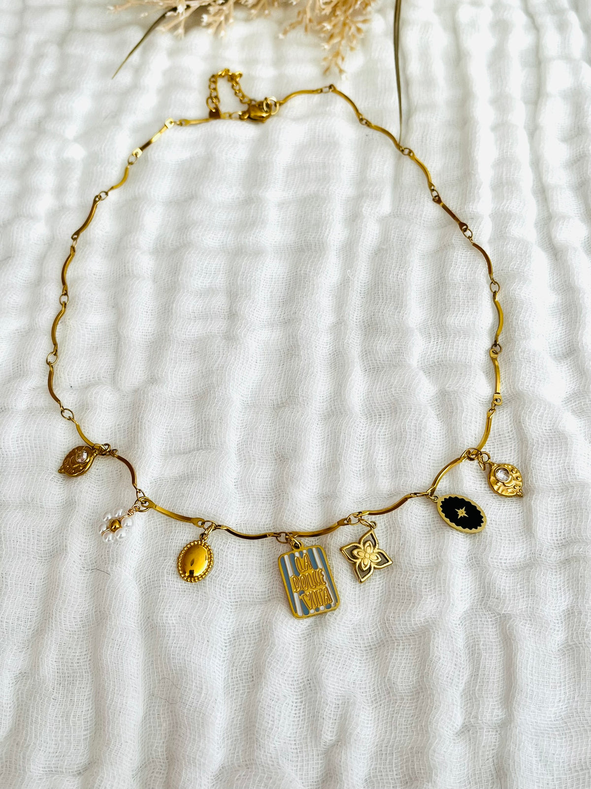 Collier fantaisie fait main.
Collier en acier inoxydable avec pampilles en nacre. Fleur, étoile, trèfle, limule en acier doré.
Pendentif central rectangle rayé rouge et rose gravé "Ciao Bella"