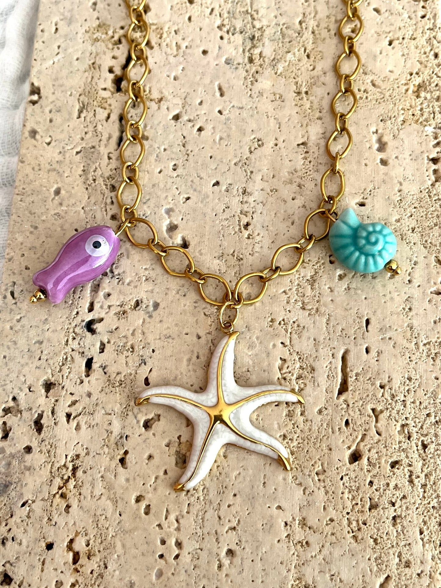 Bijou fantaisie en acier inoxydable doré fait main.
Collier gros maillons en acier inox ajustable de 42 à 47 cm.
Pendentif étoile de mer blanc nacré en acier inox.
Perle poisson violet en céramique, perle coquillage turquoise en céramique.