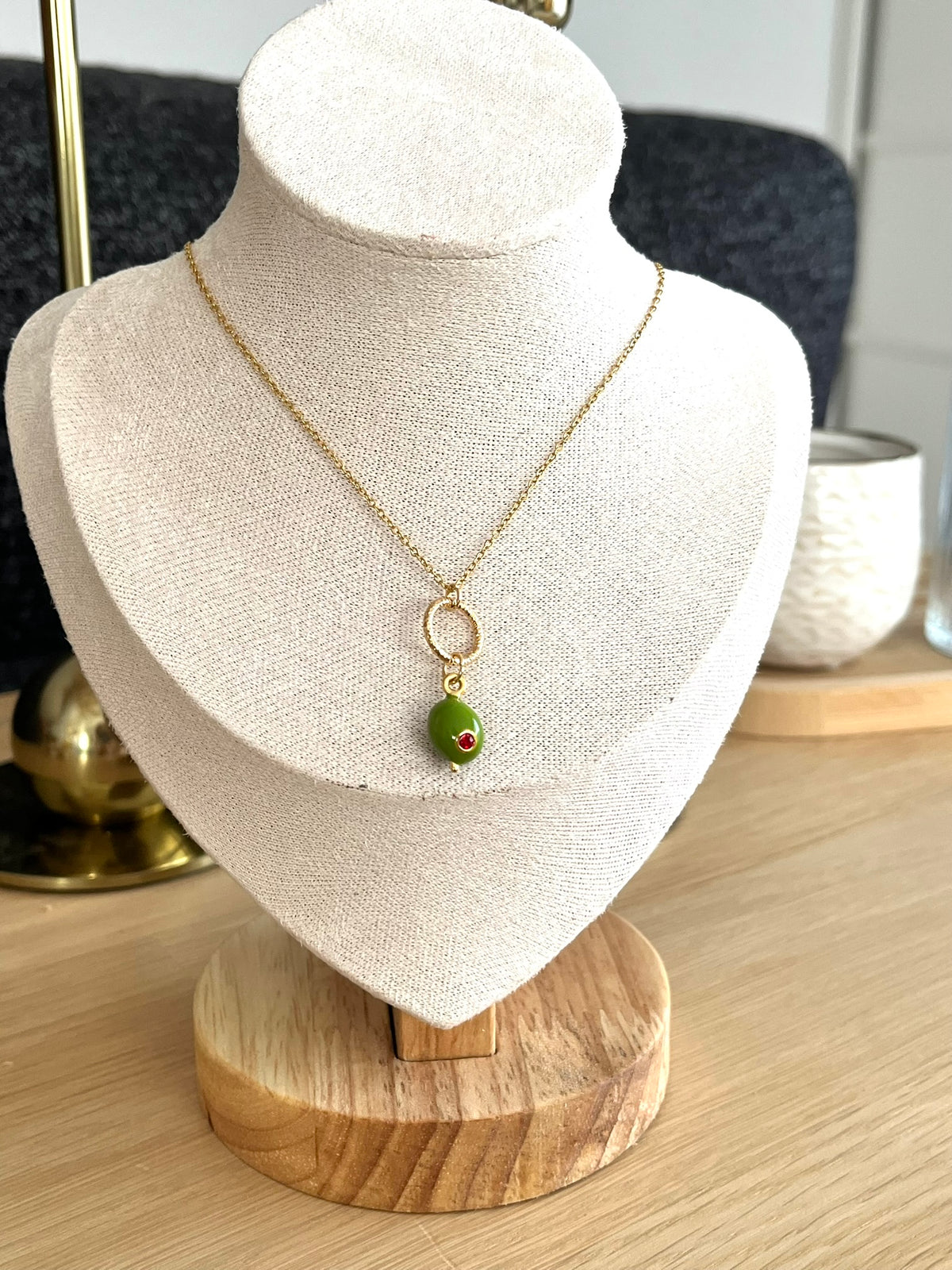 Collier fantaisie fait main
Chaîne en acier inox doré, anneau ciselé en laiton doré à l'or fin. Pendentif boule en laiton vert olive avec un strass rouge.
Bijou fantaisie fait main.