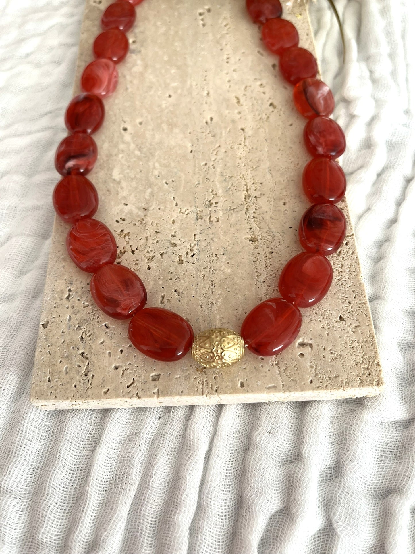 Collier fantaisie fait main.
Collier  de perles ovales en résine rouge marbré.
Perle centrale ouvragée en acier inoxydable doré.
Bijou fantaisie fait main 