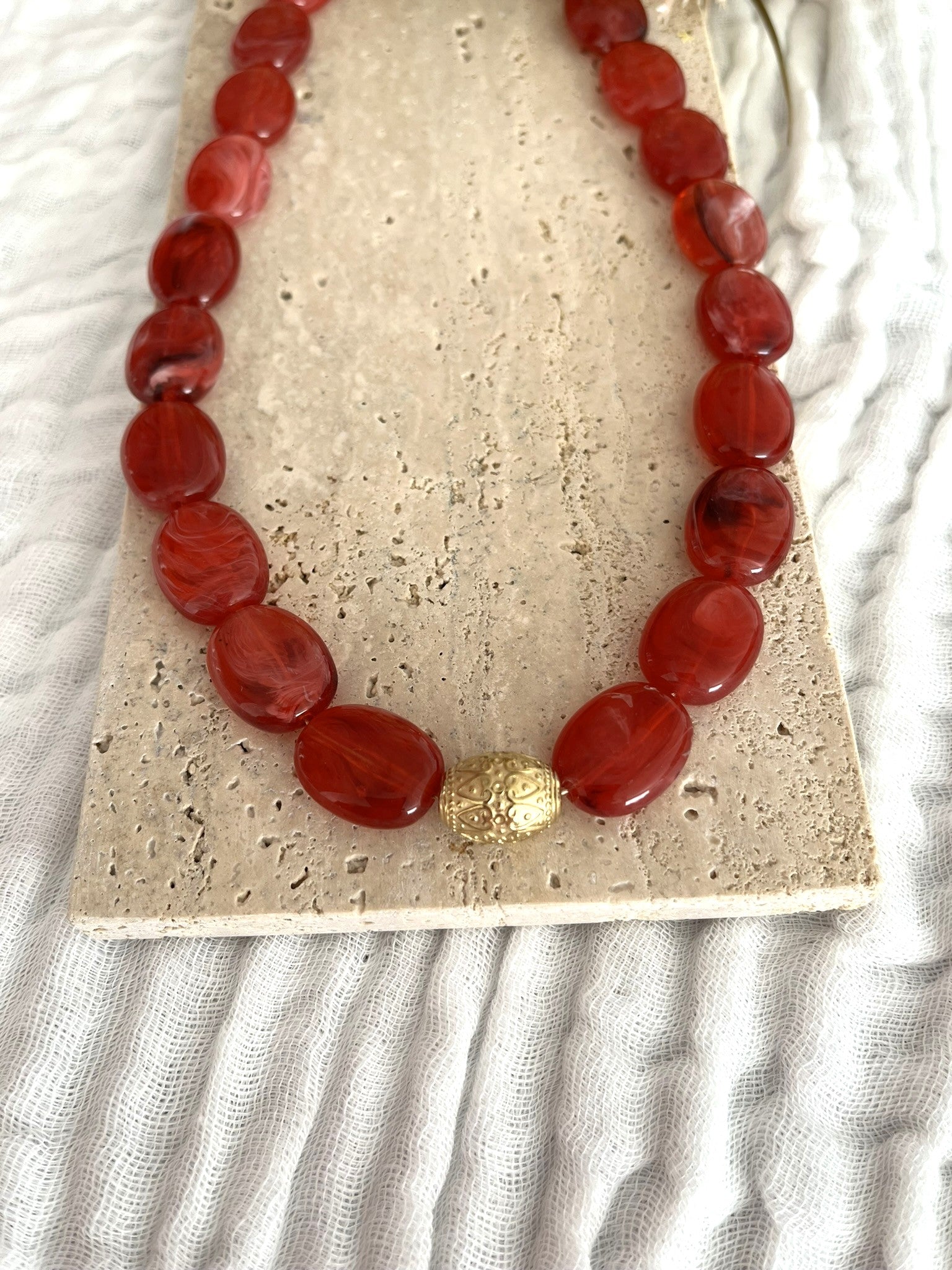 Collier fantaisie fait main.
Collier  de perles ovales en résine rouge marbré.
Perle centrale ouvragée en acier inoxydable doré.
Bijou fantaisie fait main 