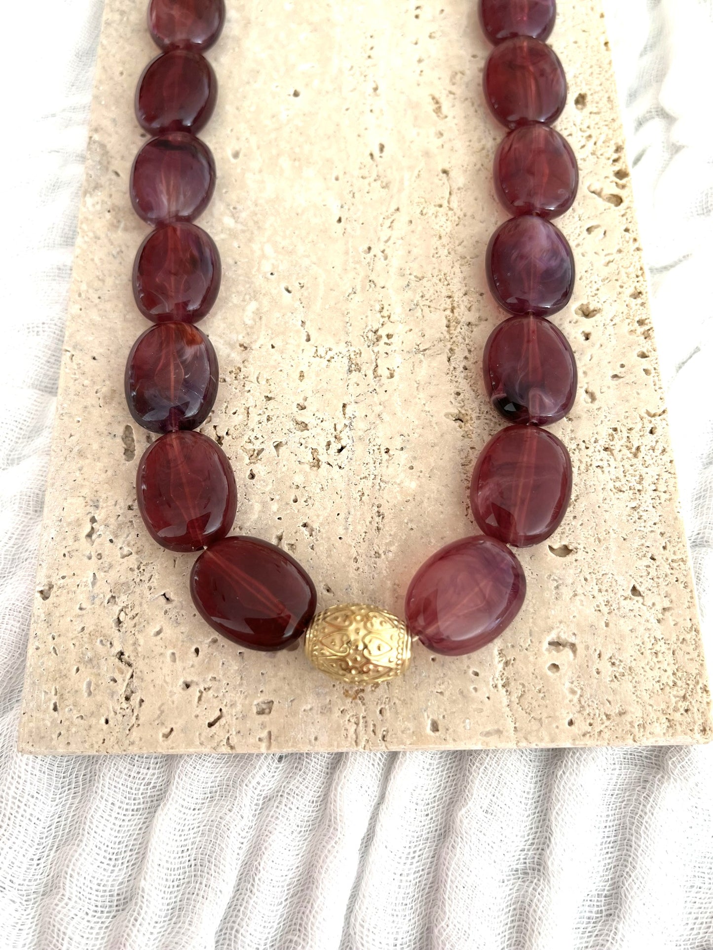 Collier fantaisie fait main.
Collier  de perles ovales en résine aubergine marbré.
Perle centrale ouvragée en acier inoxydable doré.
Bijou fantaisie fait main 