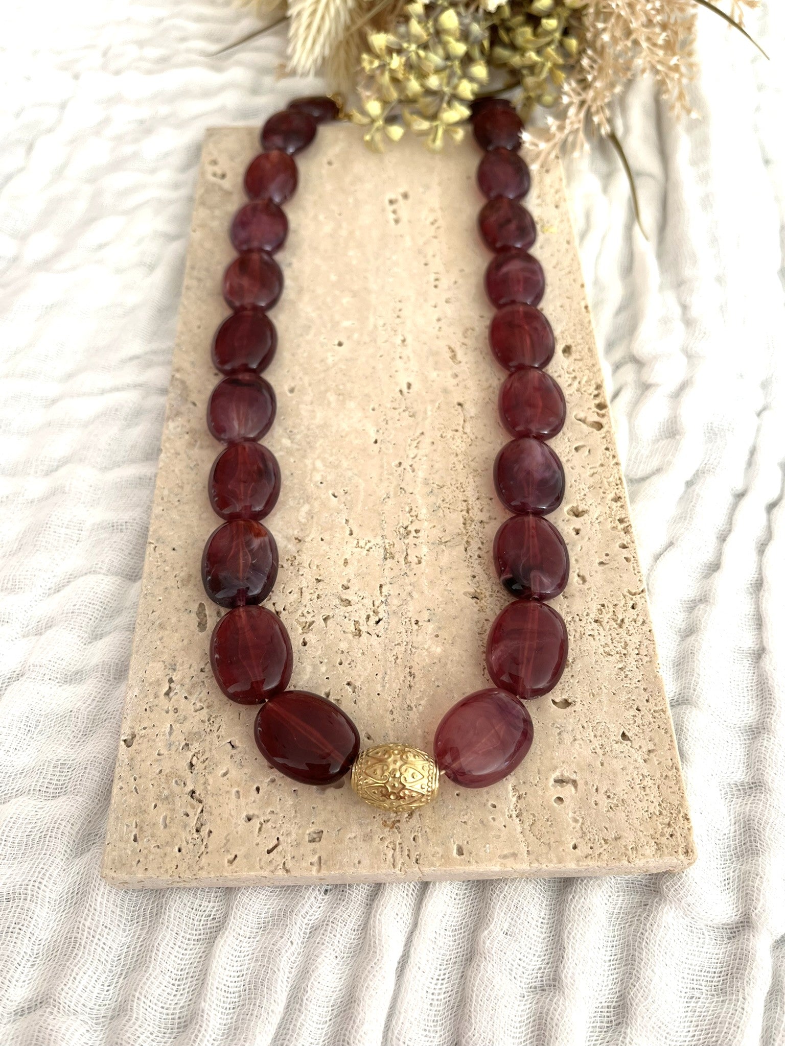 Collier fantaisie fait main.
Collier  de perles ovales en résine aubergine marbré.
Perle centrale ouvragée en acier inoxydable doré.
Bijou fantaisie fait main 