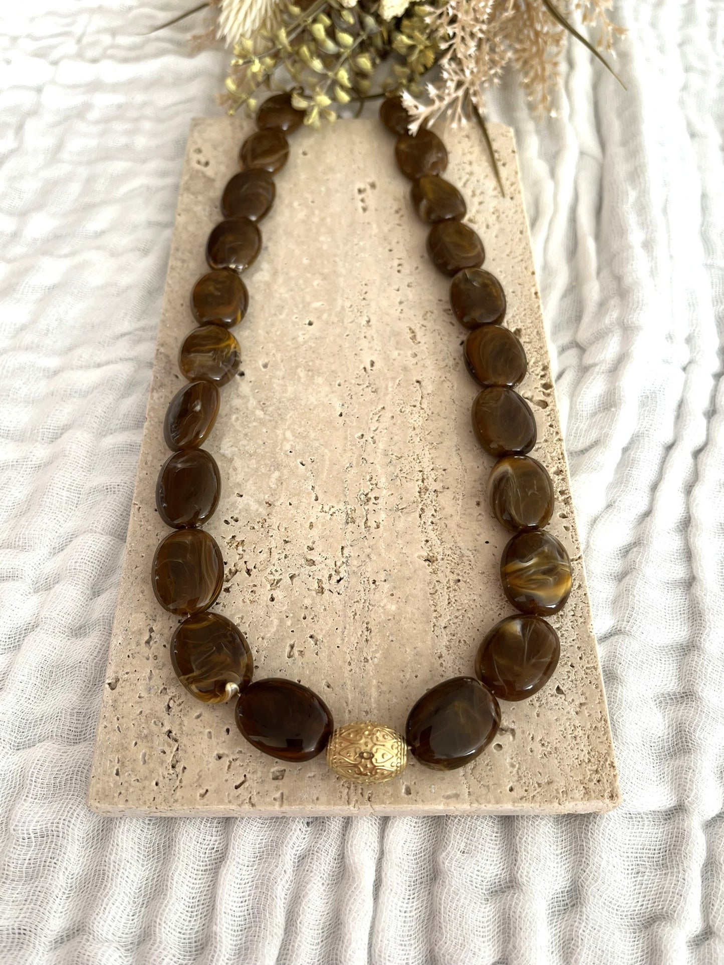 Collier fantaisie fait main.
Collier  de perles ovales en résine marron chocolat marbré.
Perle centrale ouvragée en acier inoxydable doré.
Bijou fantaisie fait main 