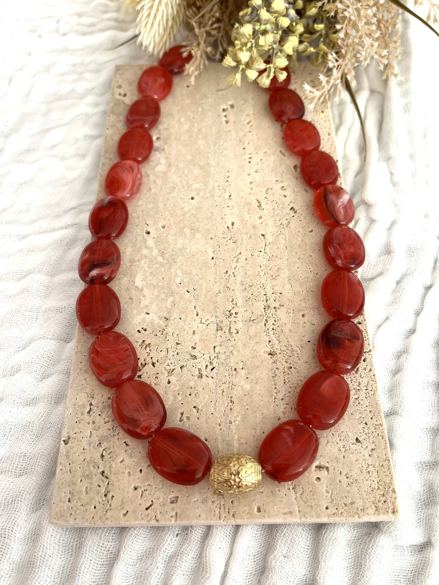 Collier fantaisie fait main.
Collier  de perles ovales en résine rouge marbré.
Perle centrale ouvragée en acier inoxydable doré.
Bijou fantaisie fait main 