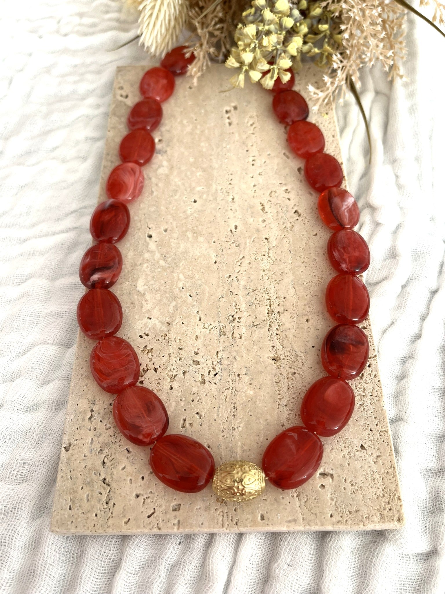 Collier fantaisie fait main.
Collier  de perles ovales en résine rouge marbré.
Perle centrale ouvragée en acier inoxydable doré.
Bijou fantaisie fait main 