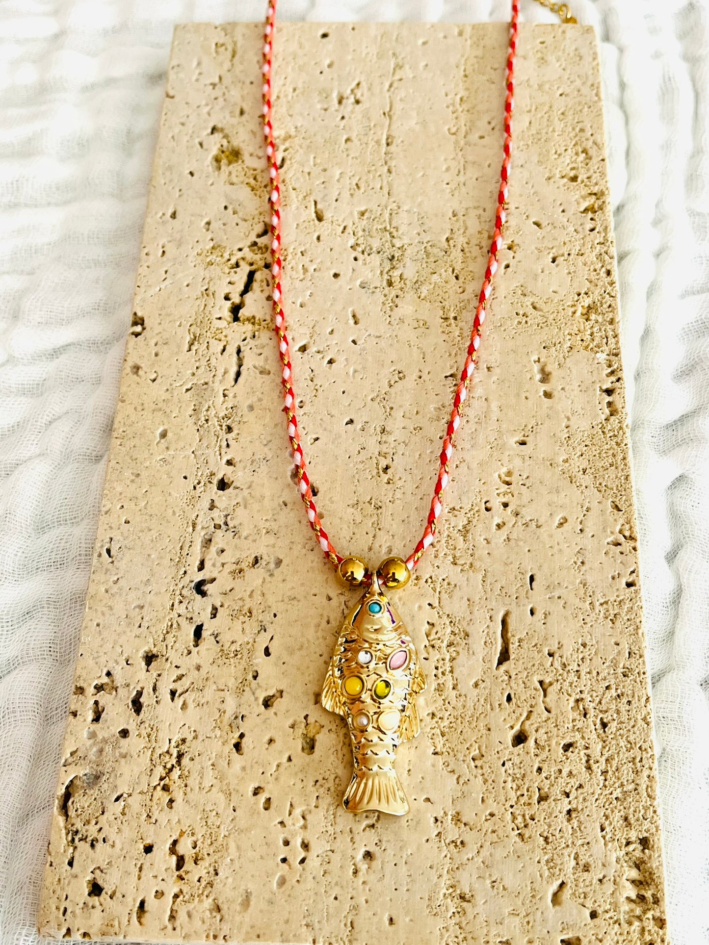 Collier fantaisie fait main.
Collier en cordon tresse en coton rouge, blanc, doré.
Pendentif poisson doré orné de pierres rose, jaune, vert.
Longueur de 41 à 46 cm.
Bijou fantaisie fait main