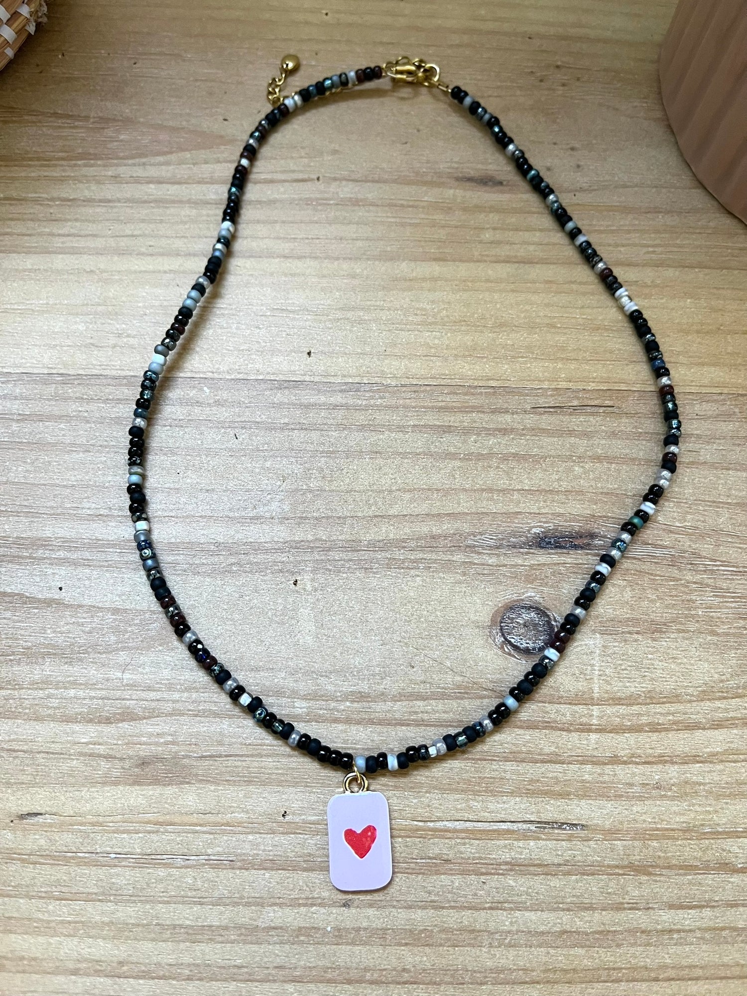Collier fantaisie fait main.
Collier ras de cou en perles de rocaille dans les tons noir, gris, argent.
Pendentif rectangulaire rose orné d'un coeur.
Bijou fait main.