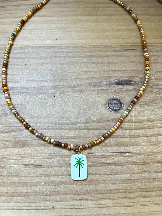 Collier fantaisie fait main.
Collier ras de cou en perles de rocaille dans les tons chauds de doré, marron, terre.
Pendentif rectangulaire blanc orné d'un palmier.
Bijou fait main.