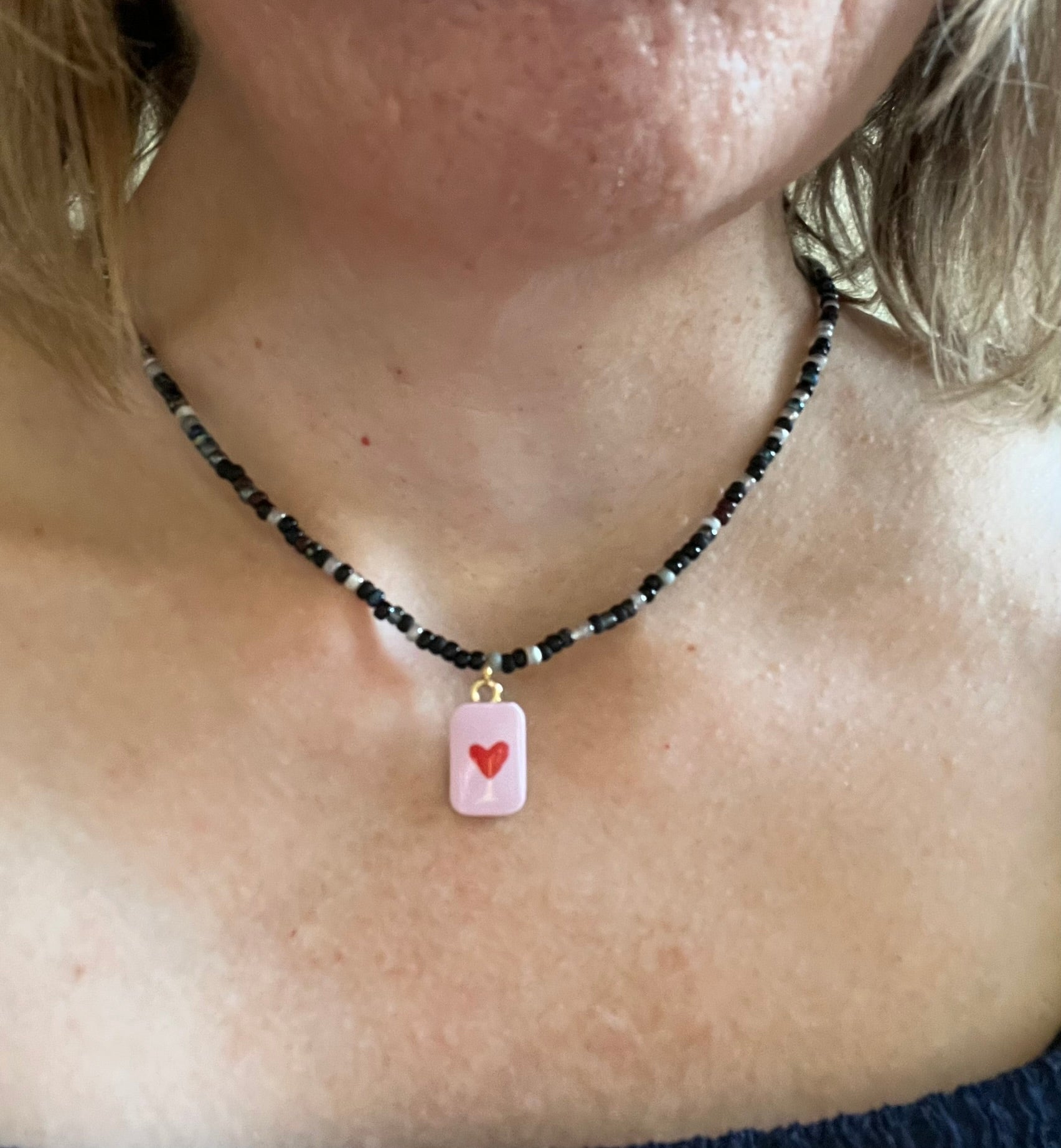 Collier fantaisie fait main.
Collier ras de cou en perles de rocaille dans les tons noir, gris, argent.
Pendentif rectangulaire rose orné d'un coeur.
Bijou fait main.
