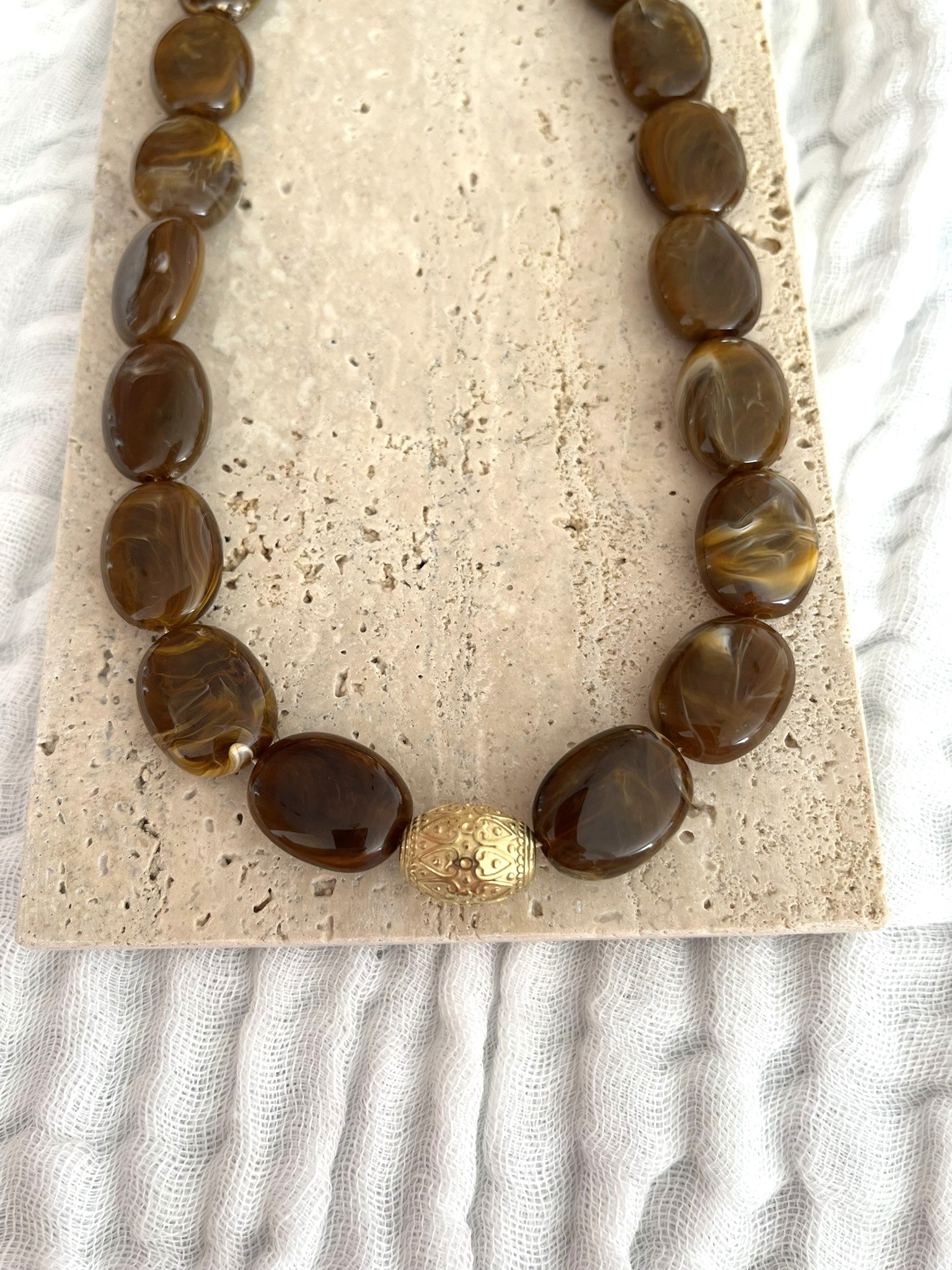 Collier fantaisie fait main.
Collier  de perles ovales en résine marron chocolat marbré.
Perle centrale ouvragée en acier inoxydable doré.
Bijou fantaisie fait main 