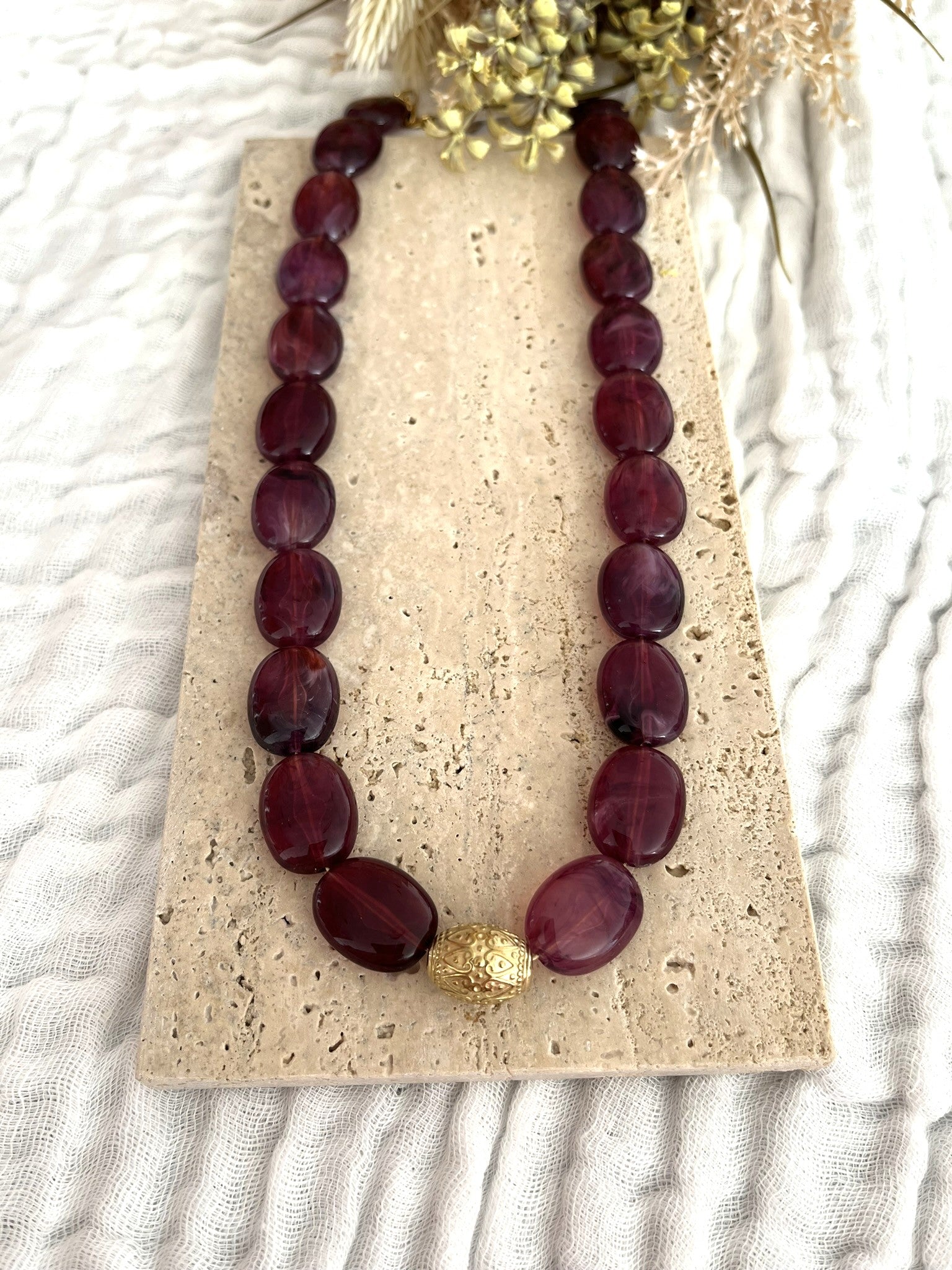 Collier fantaisie fait main.
Collier  de perles ovales en résine aubergine marbré.
Perle centrale ouvragée en acier inoxydable doré.
Bijou fantaisie fait main 