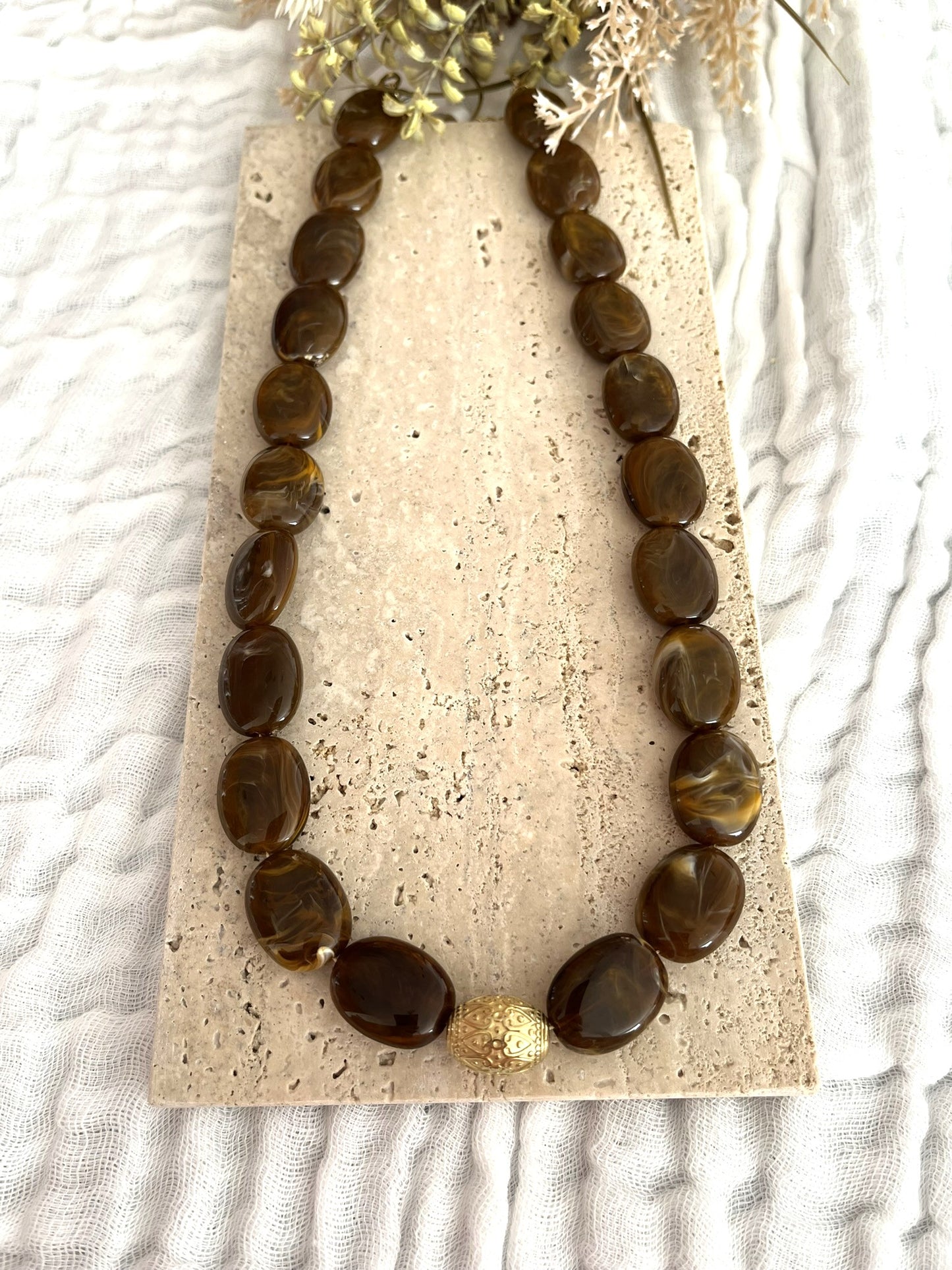Collier fantaisie fait main.
Collier  de perles ovales en résine marron chocolat marbré.
Perle centrale ouvragée en acier inoxydable doré.
Bijou fantaisie fait main 