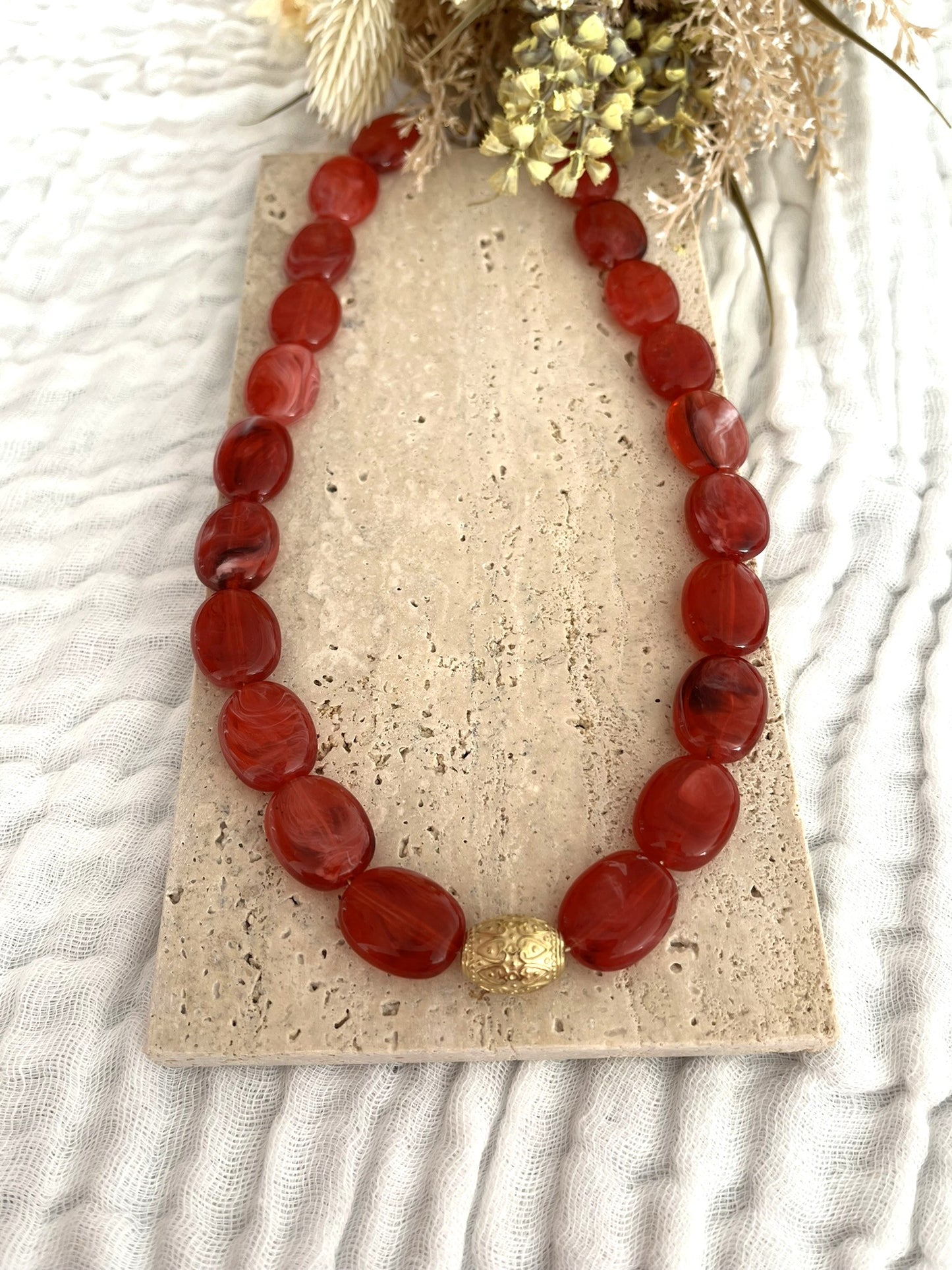 Collier fantaisie fait main.
Collier  de perles ovales en résine rouge marbré.
Perle centrale ouvragée en acier inoxydable doré.
Bijou fantaisie fait main 