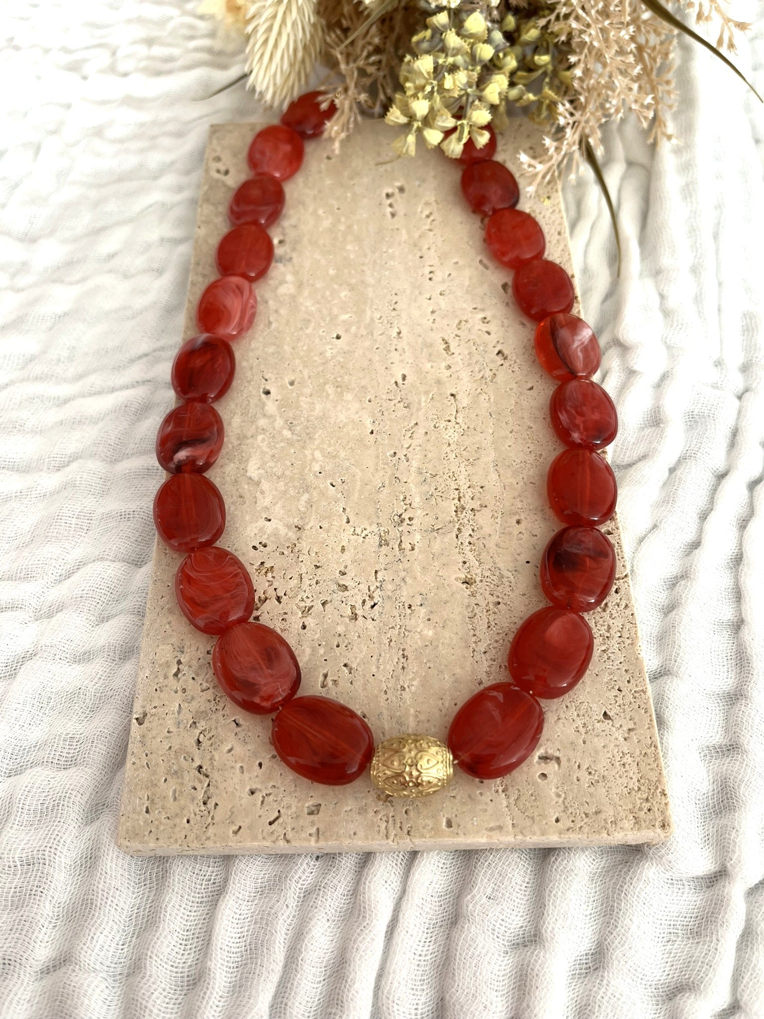 Collier fantaisie fait main.
Collier  de perles ovales en résine rouge marbré.
Perle centrale ouvragée en acier inoxydable doré.
Bijou fantaisie fait main 