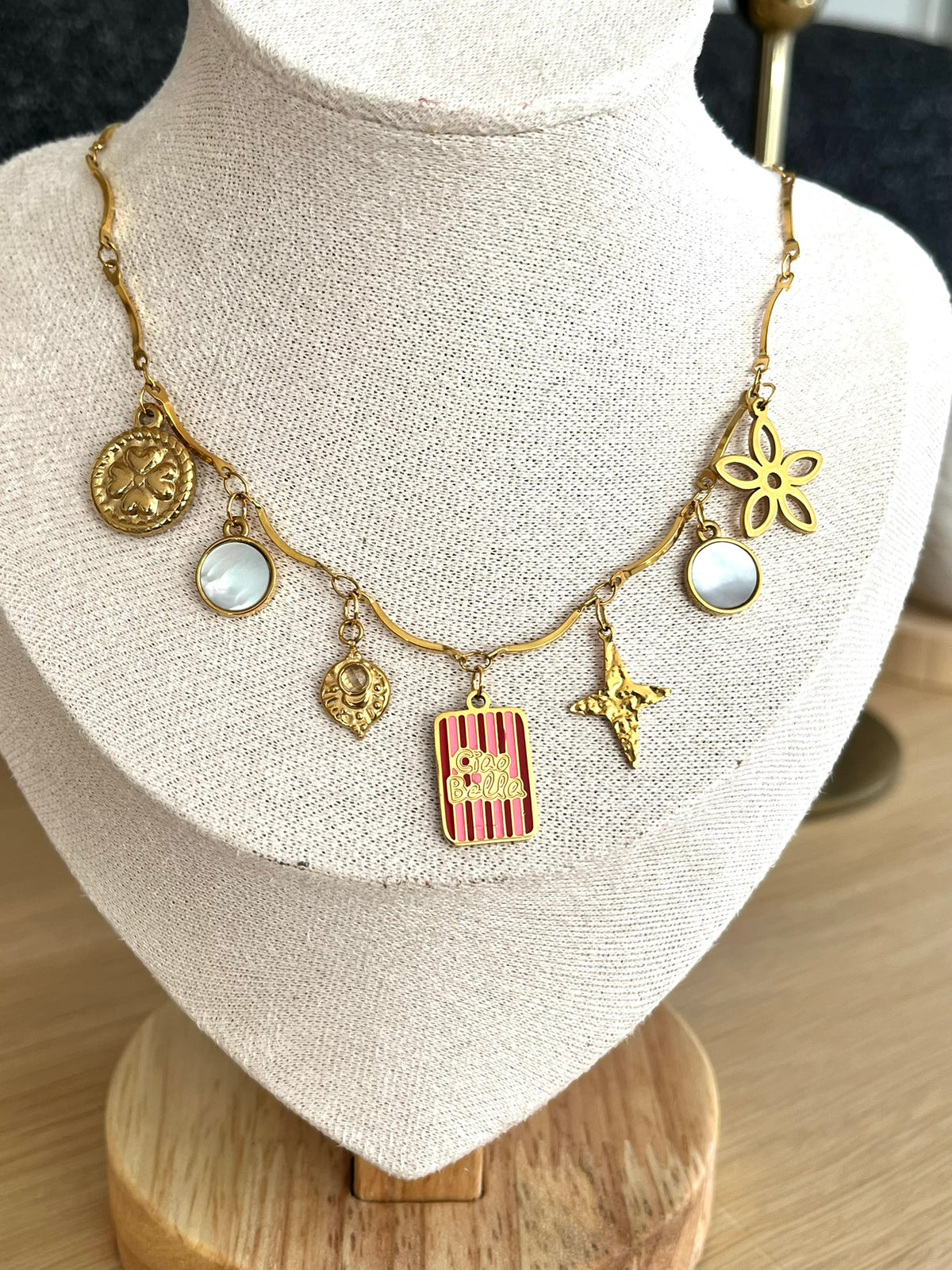 Collier fantaisie fait main.
Collier en acier inoxydable avec pampilles en nacre. Fleur, étoile, trèfle, limule en acier doré.
Pendentif central rectangle rayé rouge et rose gravé "Ciao Bella"