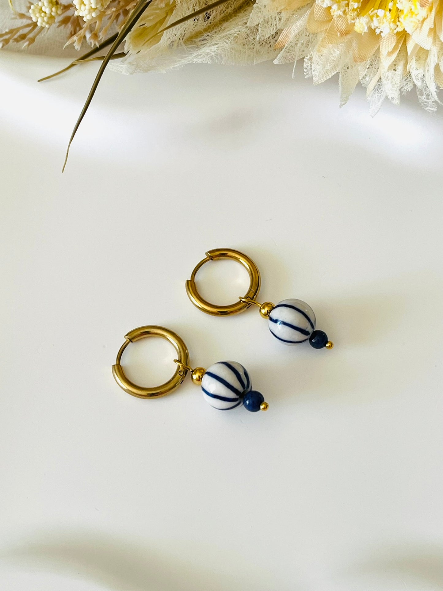 Boucles d'oreilles fantaisie fait main.
Créoles en acier inoxydable doré. Perle ronde en céramique blanche rayée bleu.
Bijou fait main