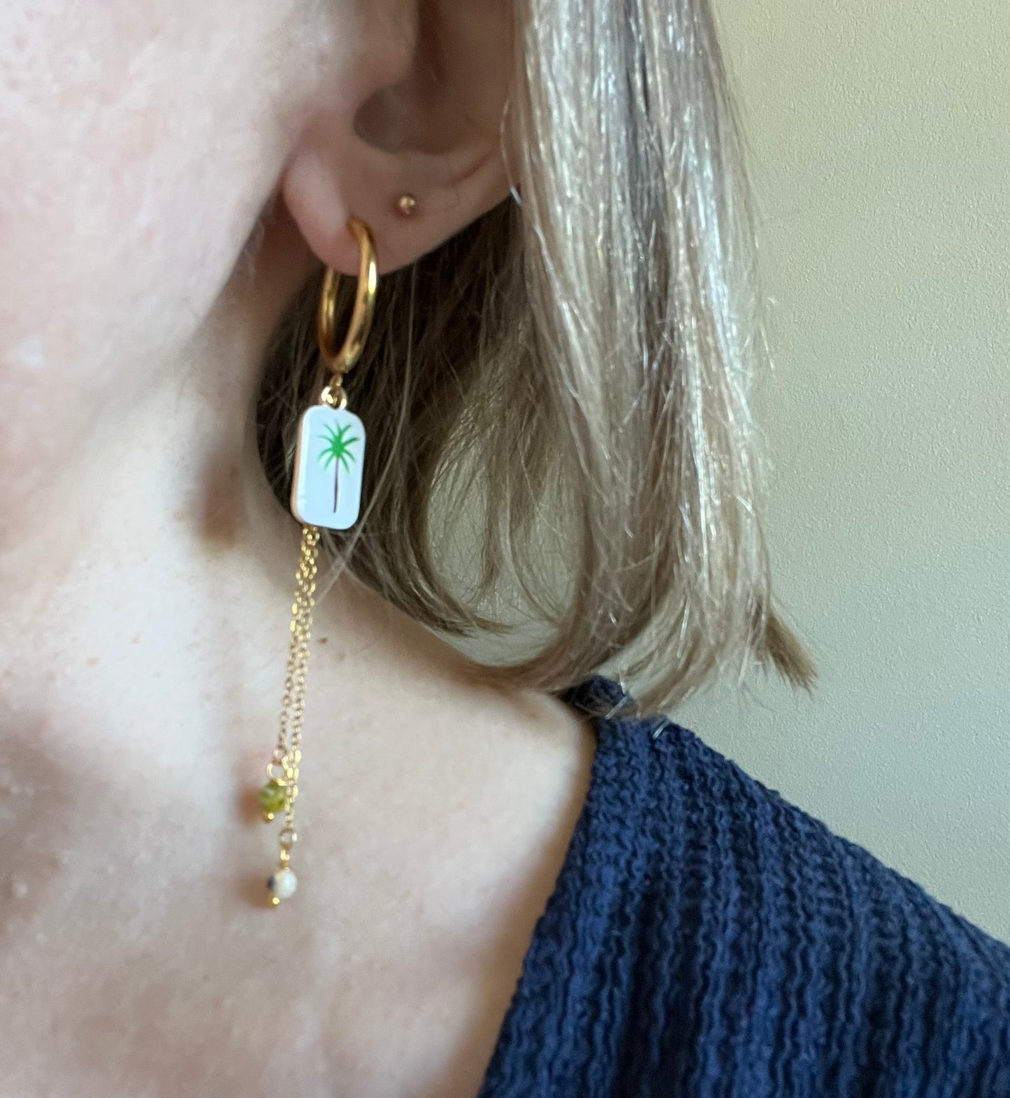 Boucles d'oreilles fantaisie fait main.
Créoles en acier doré.
Pendentif rectangle blanc orné d'un palmier vert.
2 Chainettes de longueur asymétrique réhaussées de perles millefiori dans les tons vert.
Bijou fait main