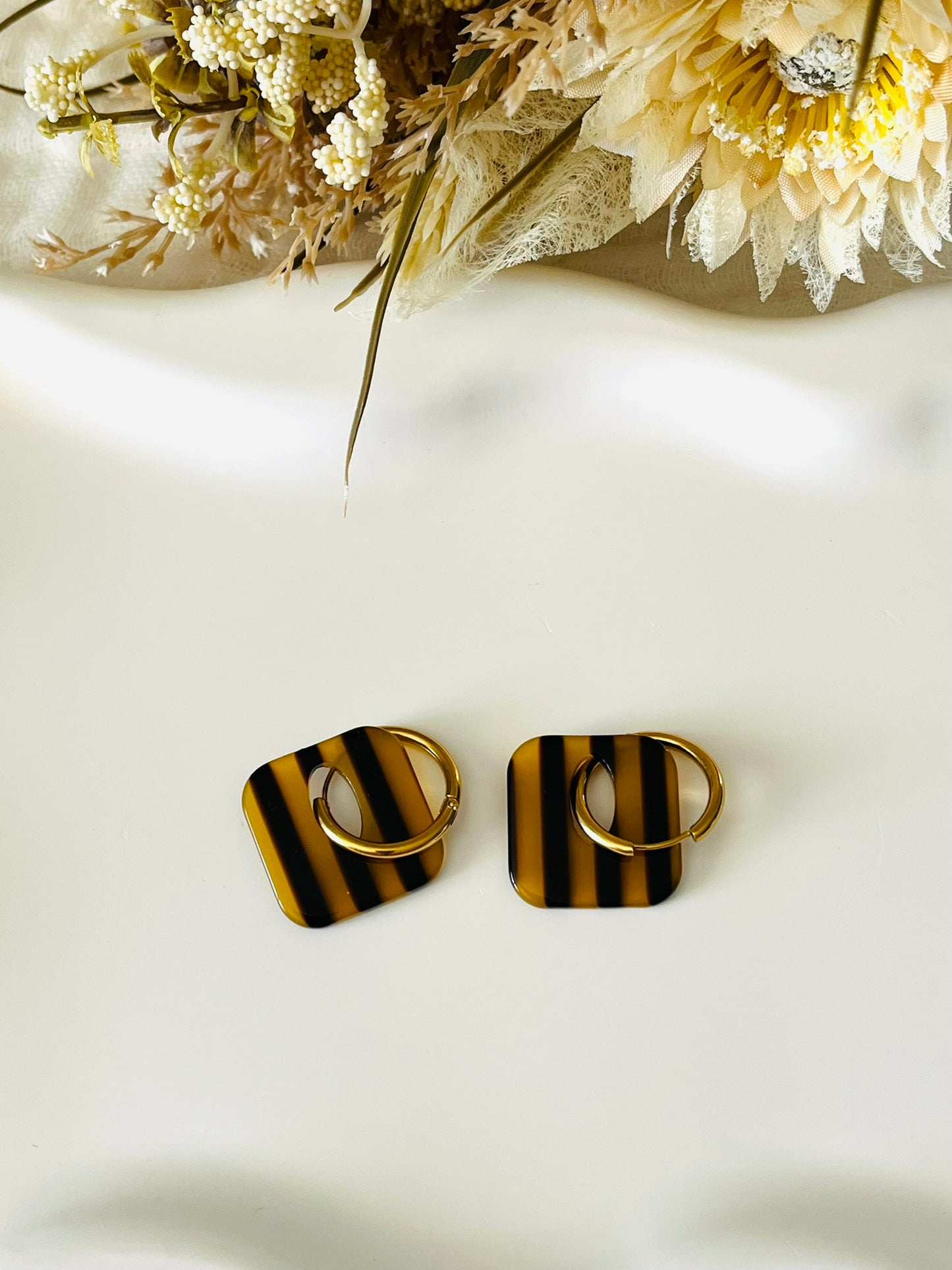 Boucles d'oreilles fantaisie fait main.
Créoles en acier inoxydable avec pampilles interchangeables.
Pampilles carrées bicolores rayées marron transparent et foncé.
Bijou fantaisie fait main.