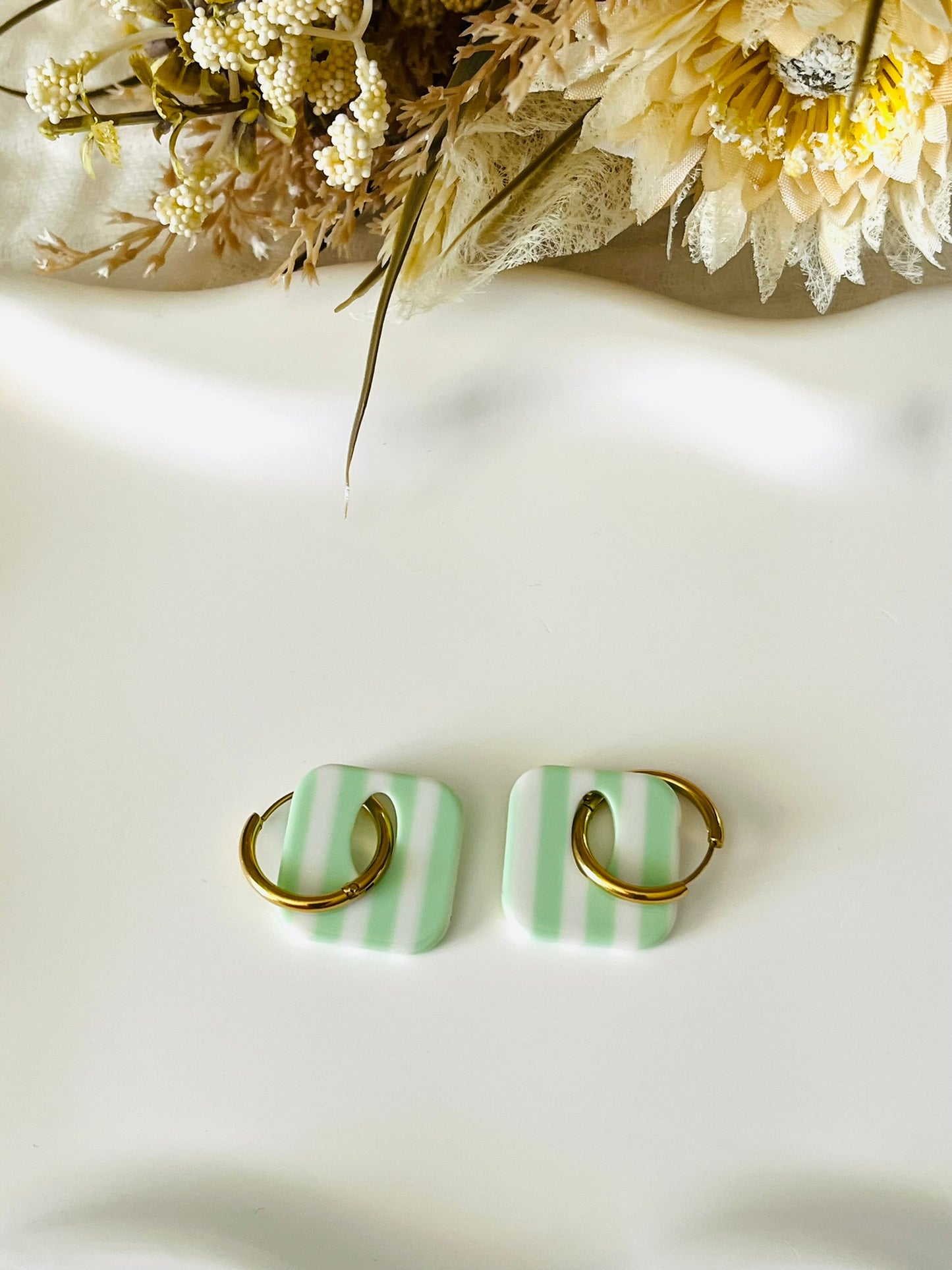 Boucles d'oreilles fantaisie fait main.
Créoles en acier inoxydable avec pampilles interchangeables.
Pampilles carrées bicolores rayées vert clair et écru.
Bijou fantaisie fait main.