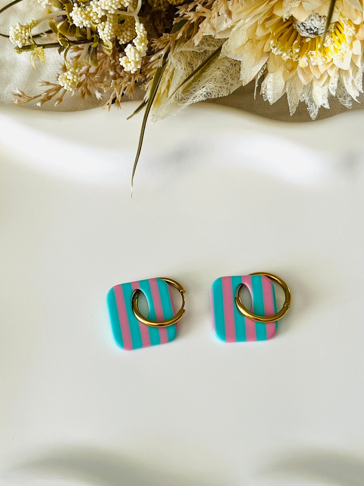 Boucles d'oreilles fantaisie fait main.
Créoles en acier inoxydable avec pampilles interchangeables.
Pampilles carrées bicolores rayées turquoise et rose.
Bijou fantaisie fait main.